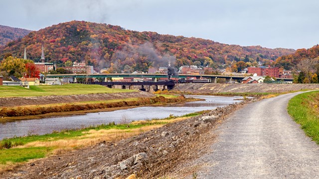 Train passing through a railroad town in front of red, yellow, and orange mountain foliage 