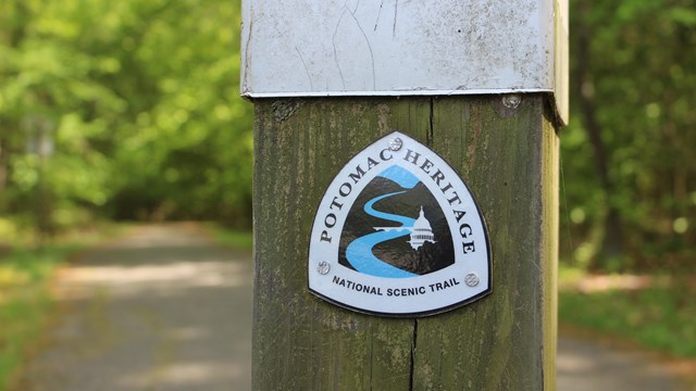 A trail marker on a wooden post adjacent to a paved path.