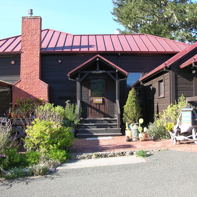 A photo of the main entrance to a one-story, brown-sided, red-roofed building.