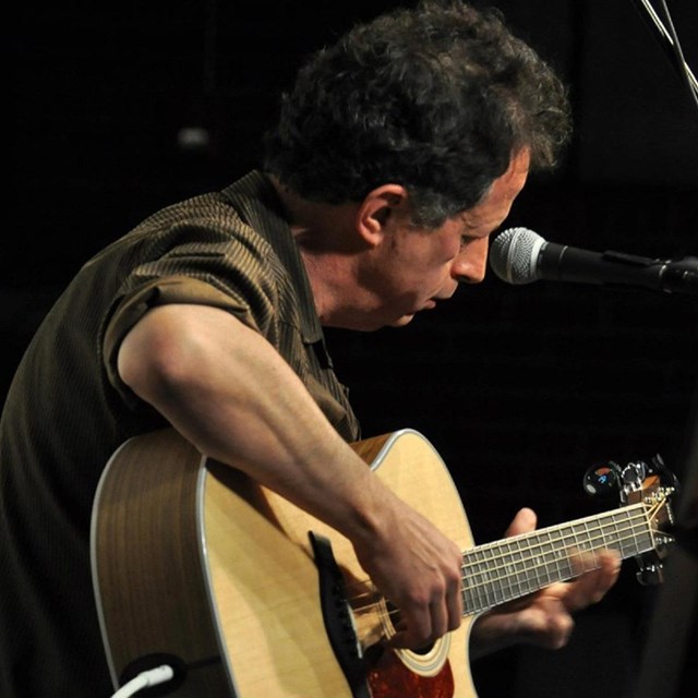 A man plays acoustic guitar into a microphone