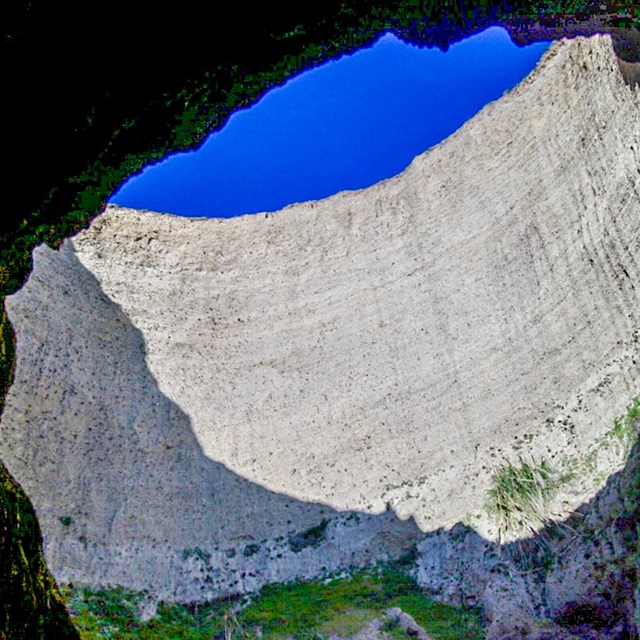 Looking up at blue sky visible through a large circular hole in the roof of a sea cave.