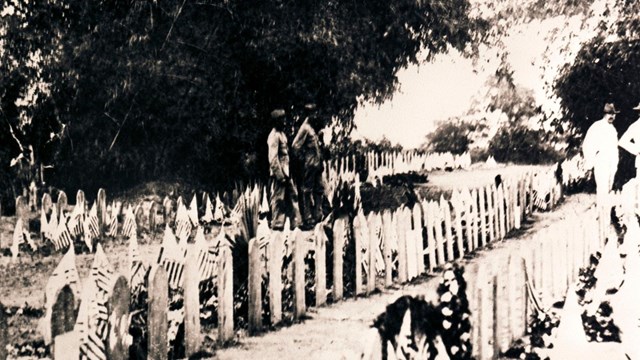 B&W photo of two men standing in cemetery with american flags