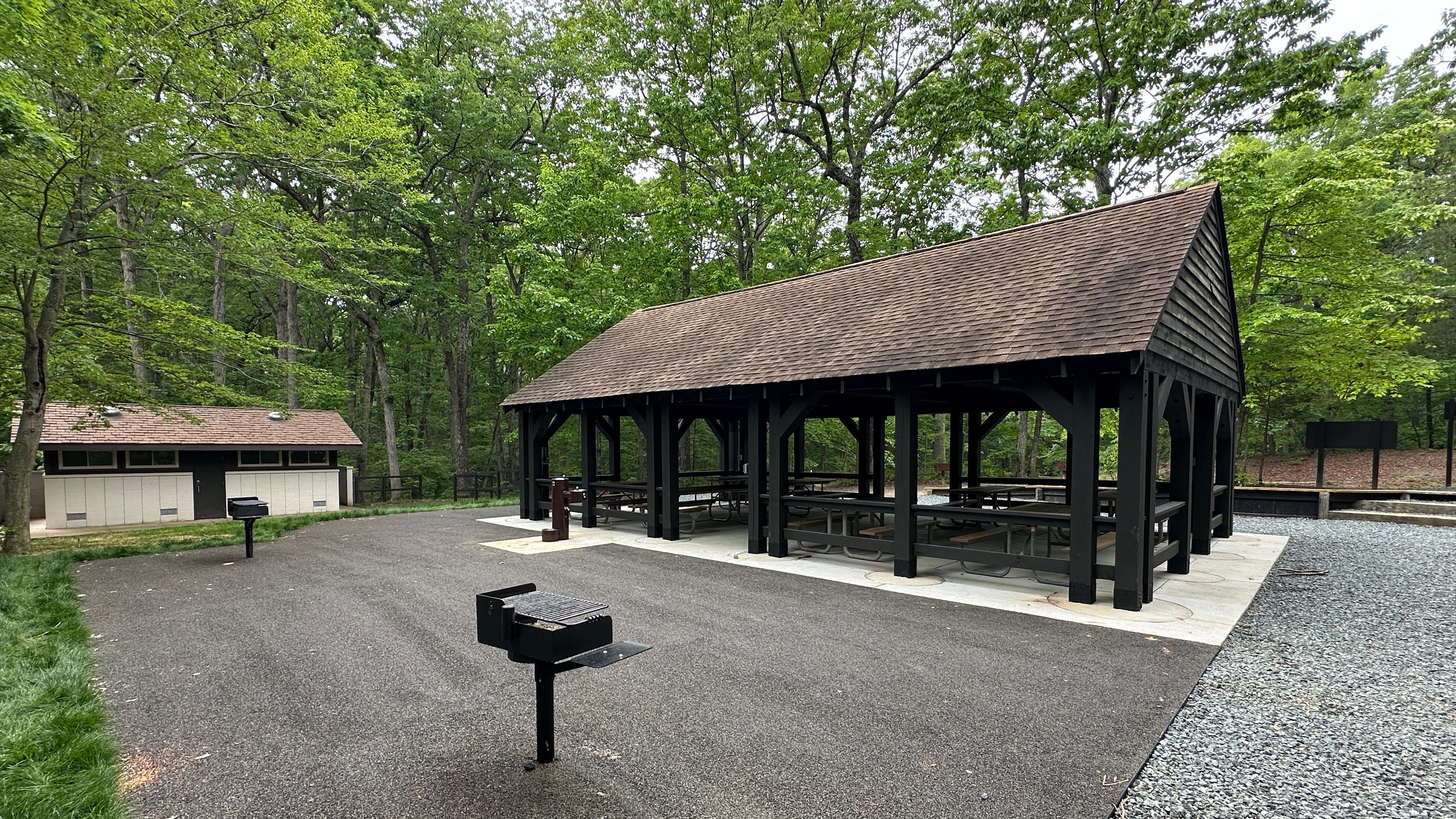 Wooden pavilion with picnic tables near a paved pad with two grills and a water fountain