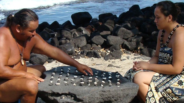 Two people in traditional clothing play a game of kōnane