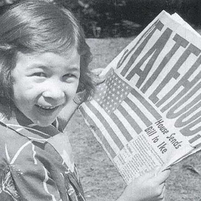 Historic photo of excited girl holding newspaper that says 