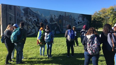 Group of students listen to a ranger in front of a Pullman mural.
