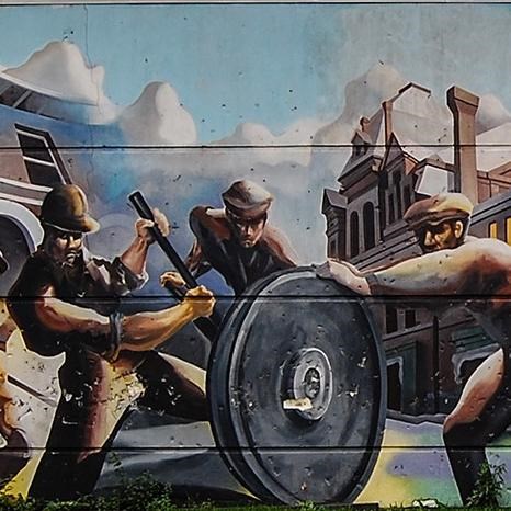 Colorful mural on the back of a building showing workers, historic buildings, and Pullman train. 
