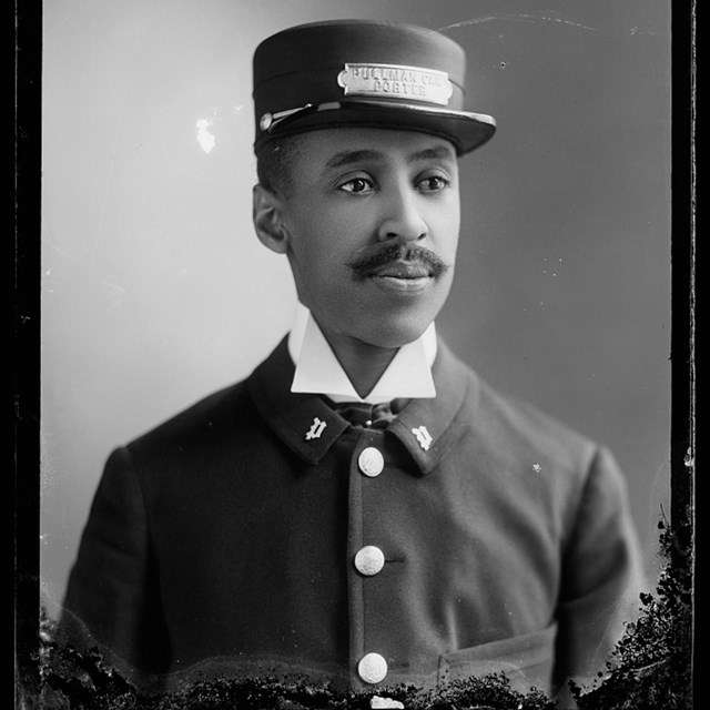 A photo portrait of a black man wearing a hat that is plated 