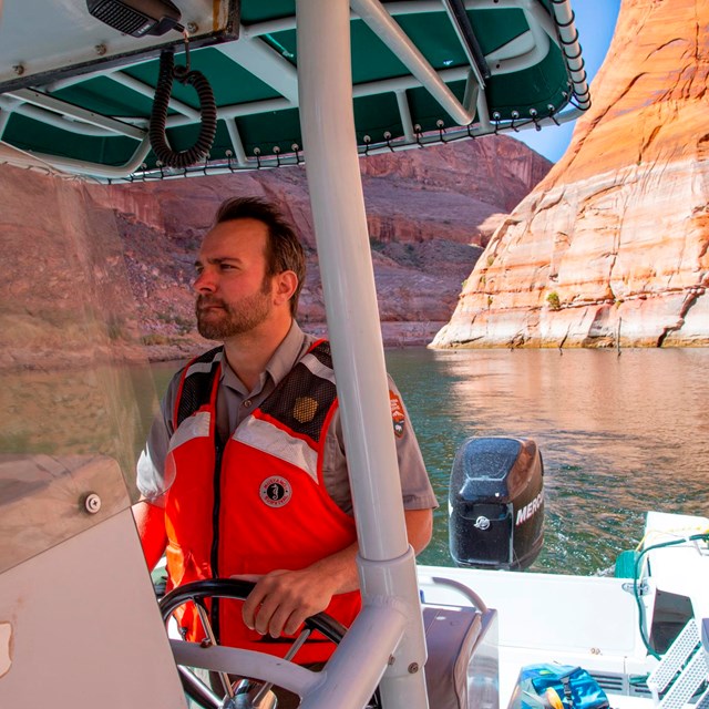 Ranger in life jacket drives motor boat in canyon at wakeless speed 