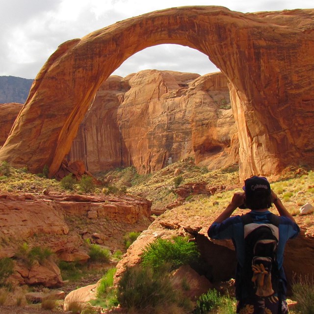 A person has his back to Rainbow Bridge as he takes a picture.