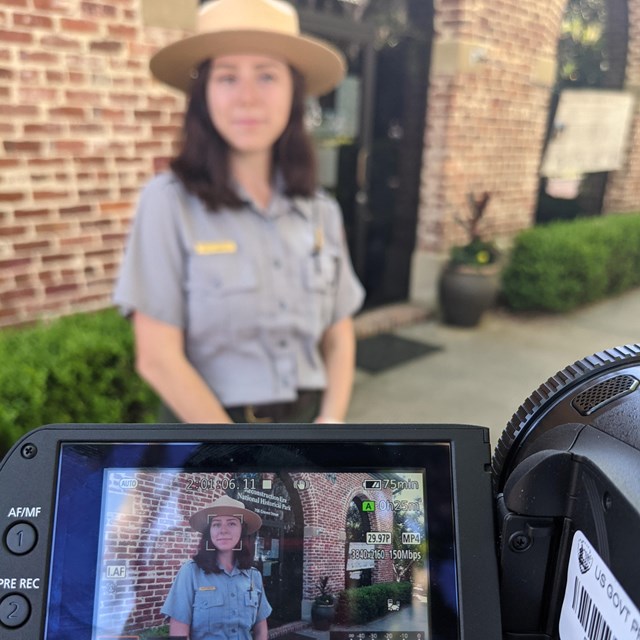 A ranger stands behind a video camera.