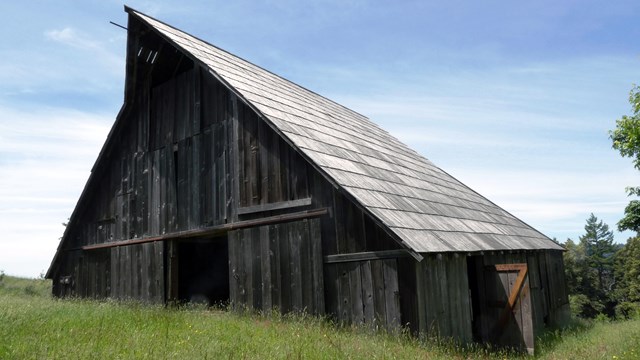 A brown wooden barn on a  grassy slope