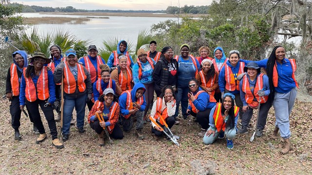 A large group of people in safety vests stand in front of a marsh view.