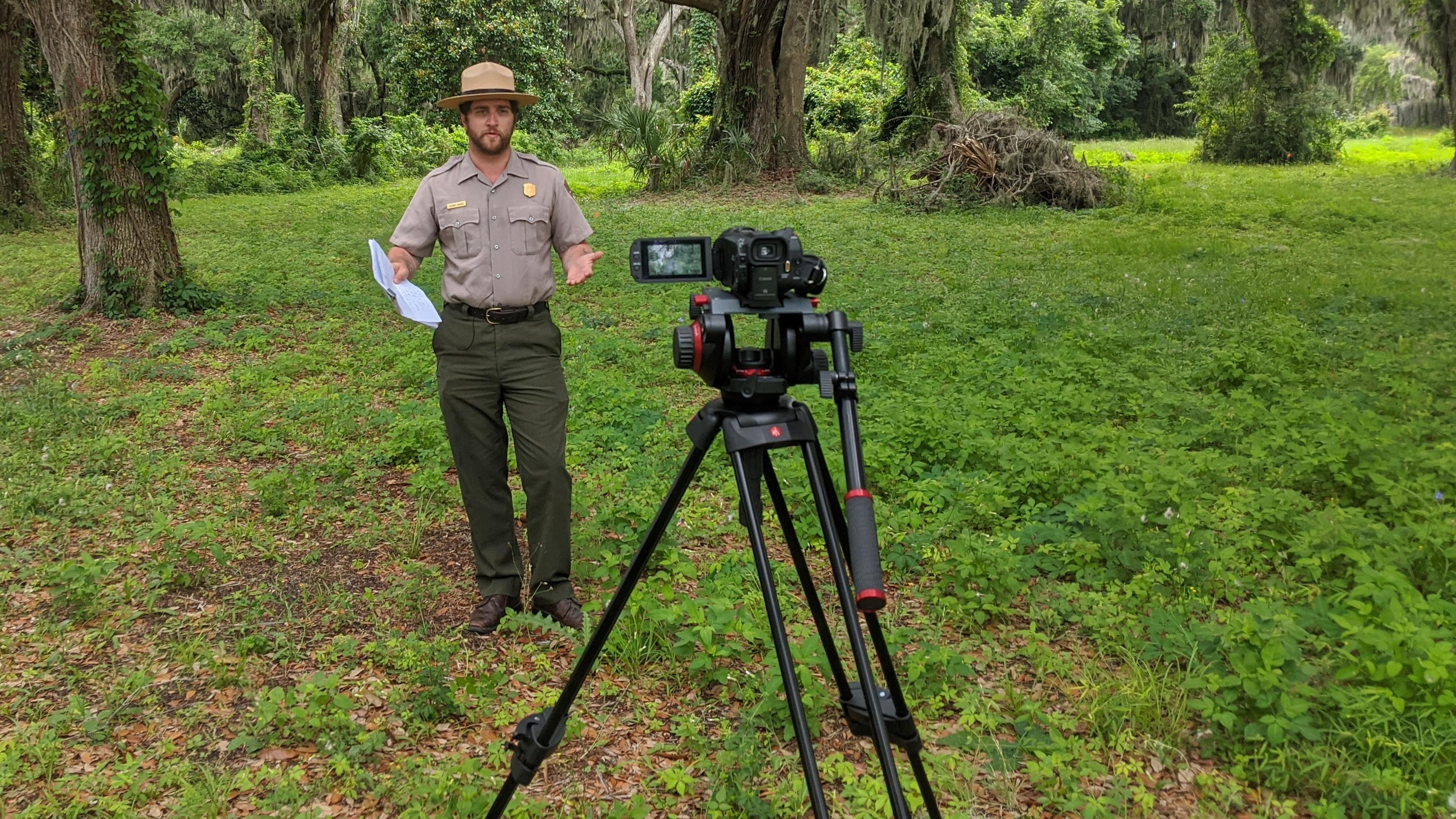 A ranger in a grove of oak trees talking to a camera in foreground