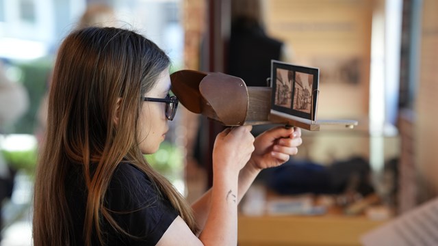 A young girl looks through a wooden stereoscope at a picture.