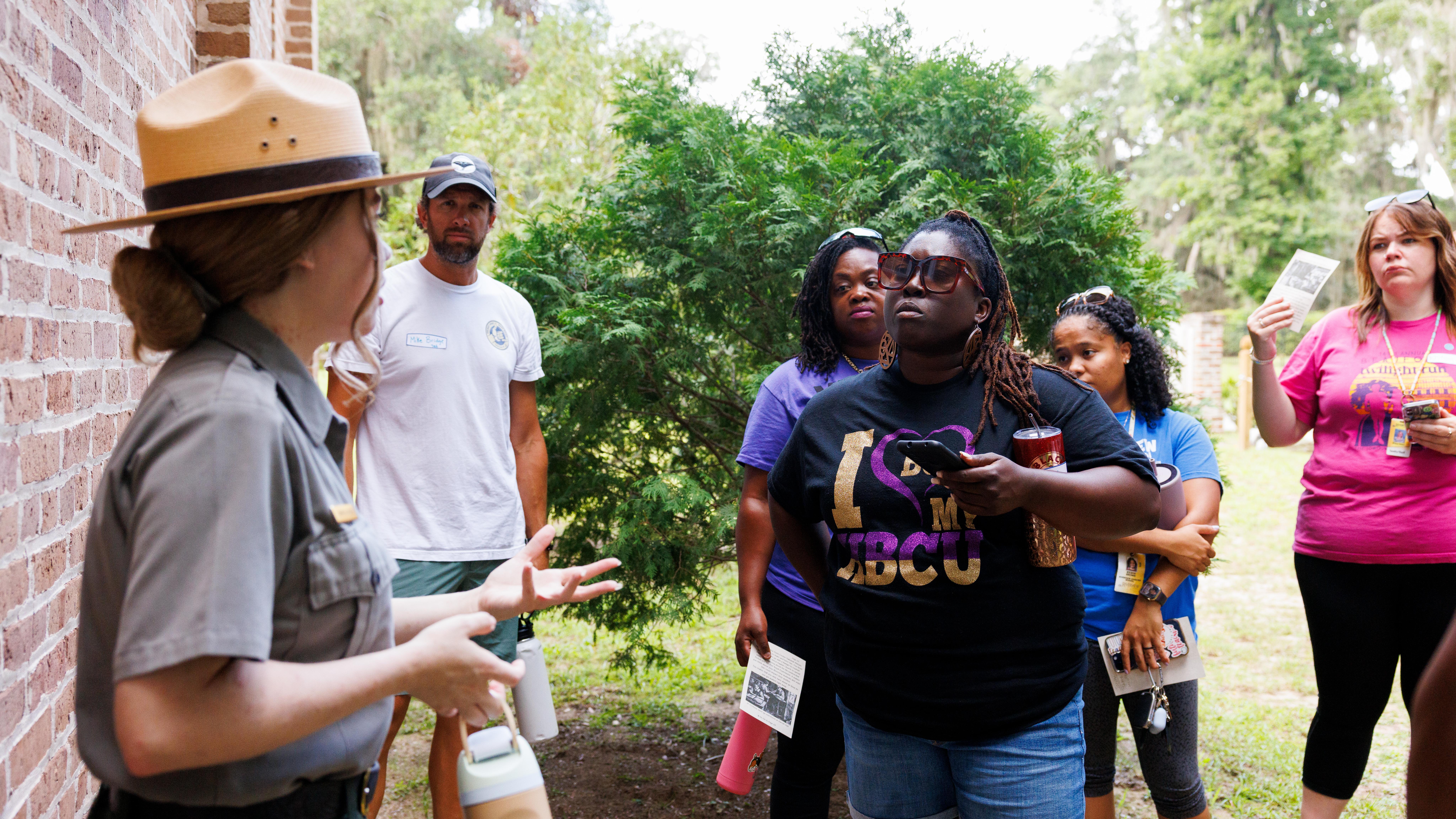 A ranger talks to a group of adults in front of a brick wall.