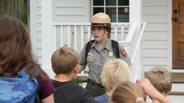 A ranger talks to a group of students in front of a white chapel.