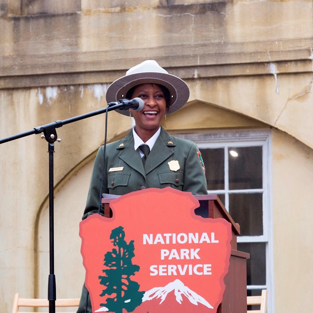 A ranger stands behind a podium with a National Park Service arrowhead.