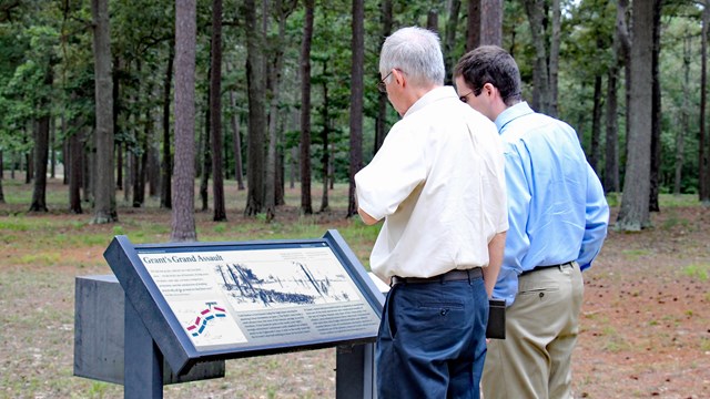 a photograph of two men examining a wayside side outdoors.