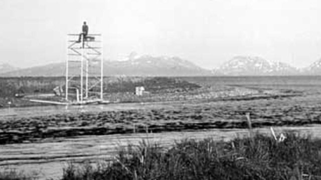 Black and white image of person sitting on structure on the bank of Delight Creek in Kenai Fjords