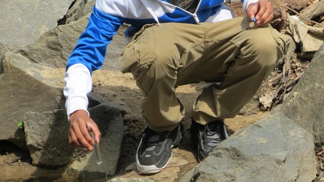 a boy crouches at the waters edge holding a test tube