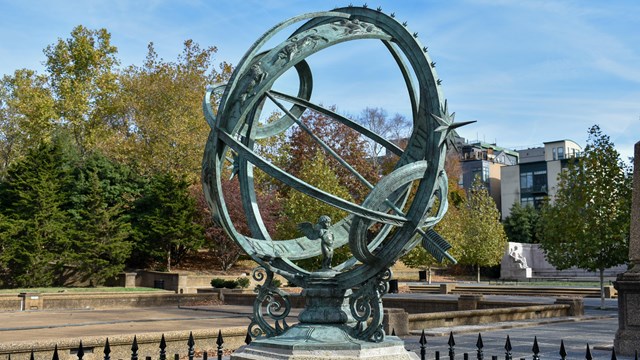 A green-tinted armillary sphere on a stone platform with a fence around it