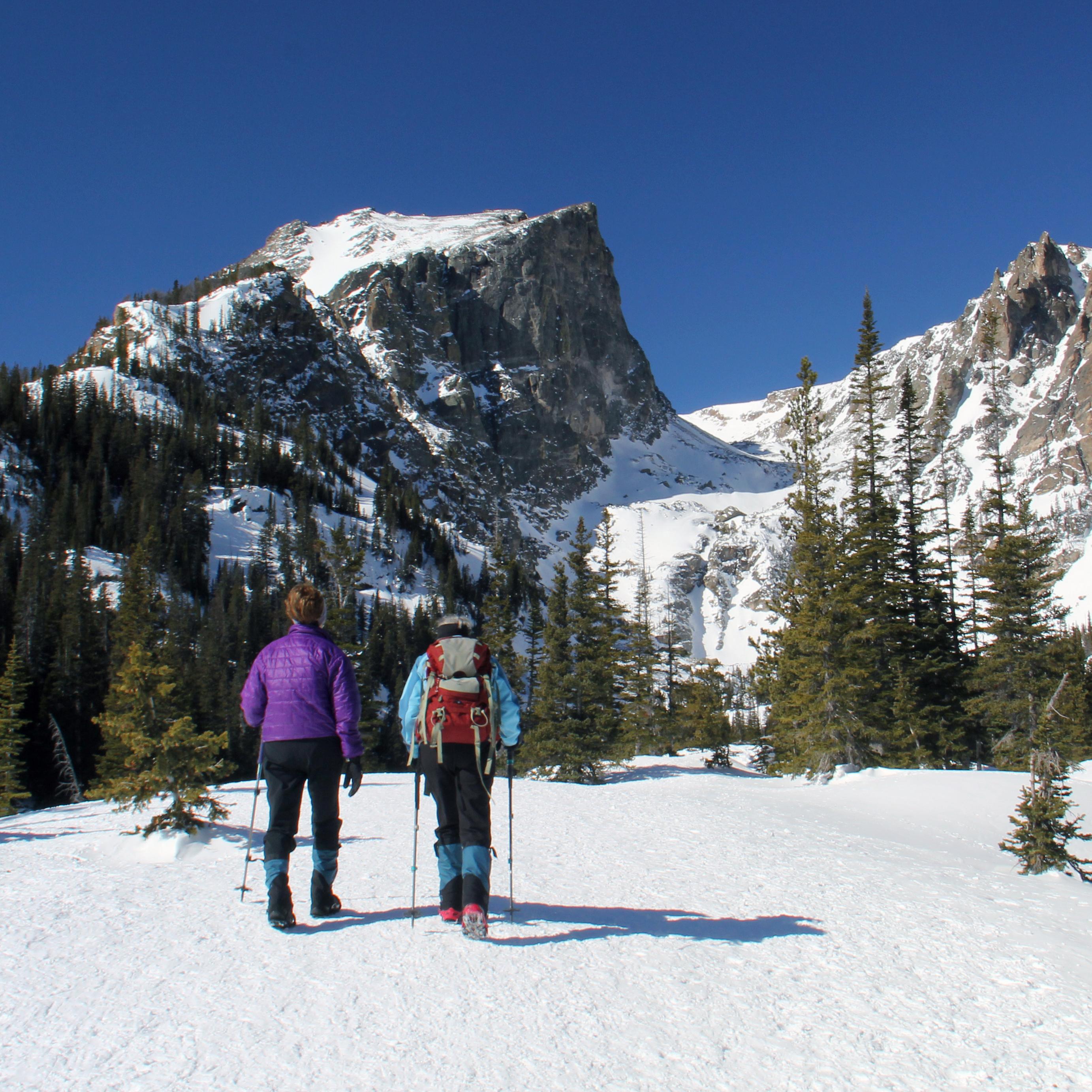 Two people are snowshoeing and carrying backpacks on a high-elevation trail covered with snow