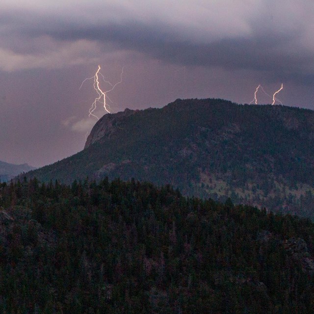 Bolts of lightning are striking down toward the top of mountain peaks