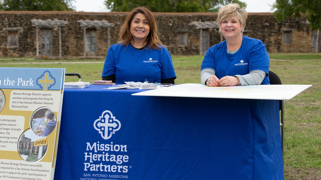 Two Mission Heritage Partner staff sit at an information booth.