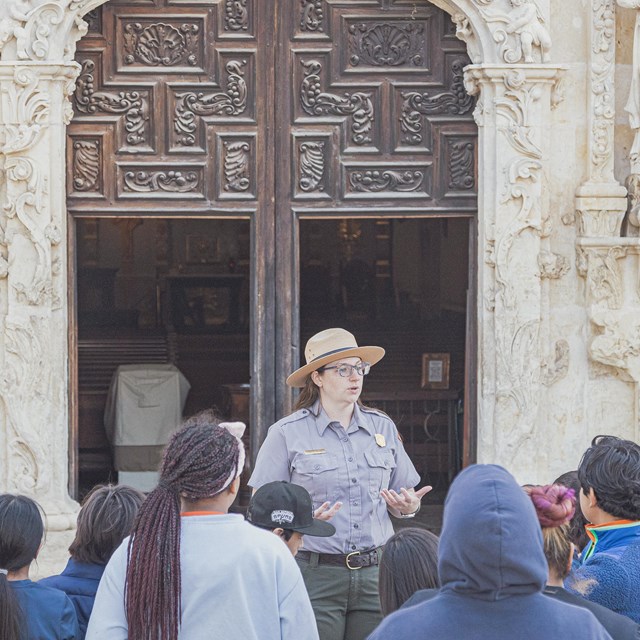 Ranger guiding school field trip with the entrance of the Mission San José church in the back. 