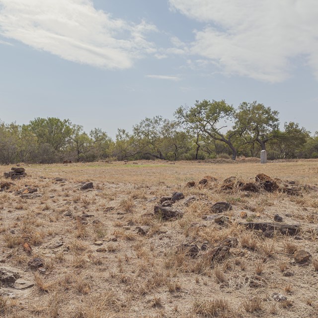 A field of yellow grass with stone foundations coming out of the ground. 