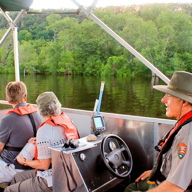 A ranger and visitors look at scenery from a boat.