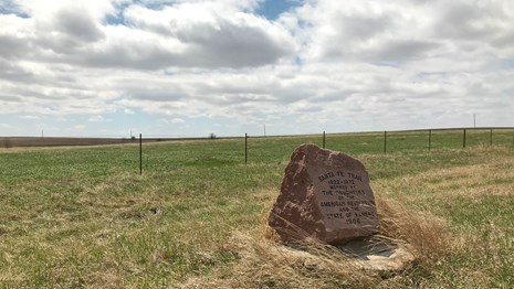 A stone monument sits in a vast flat field of mowed grass.
