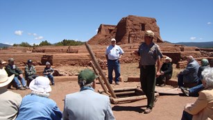 A park ranger speaks to a group of people in front of a historic adobe mission church.
