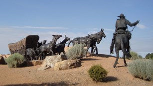 A bronze statue of a wagon being pulled by mules, with a cowboy on a horse.
