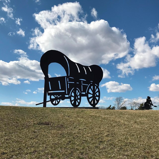 A silhouette of a covered wagon, on a grassy hill.