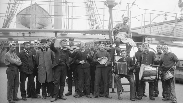 Group of men standing on the deck of a sailing ship holding various instruments