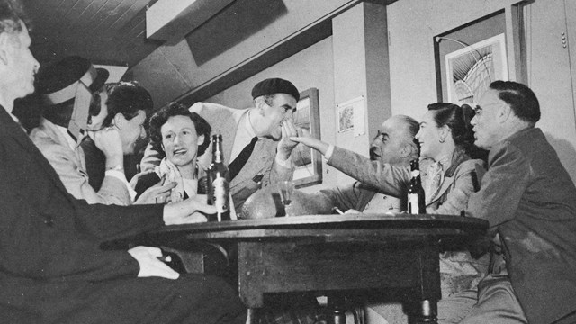 black and white photo of men and women sitting and laughing together around a table.