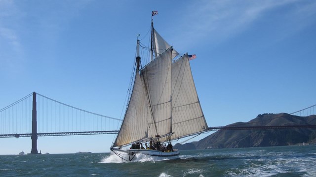 a large sailboat sailing on choppy water with the golden gate bridge in the background.