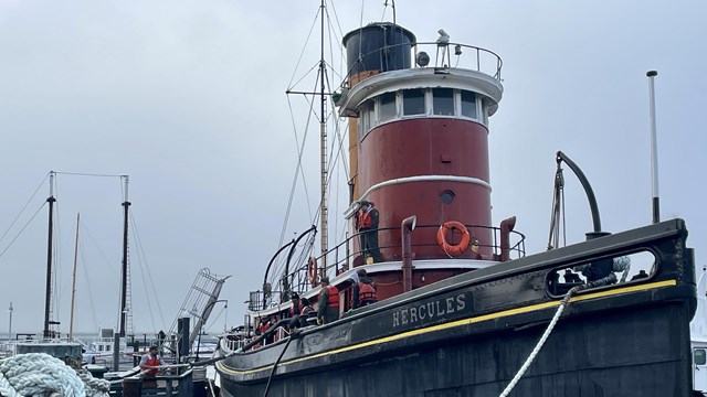 a large red steam tug boat is moored to a pier