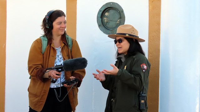 a park ranger talks to someone wearing headphones and holding a microphone.