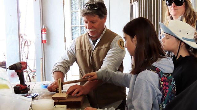A park volunteer helps a group of children make a small boat