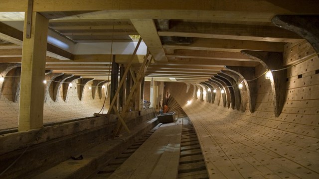Inside a ships hold, heavy wood beams and rivets being installed