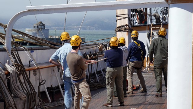 Volunteer rigging crew with helmets work aboard Balclutha