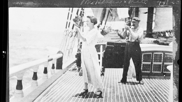 a woman in a long white dress stands on the deck of a ship holding a navigation tool up to her eye