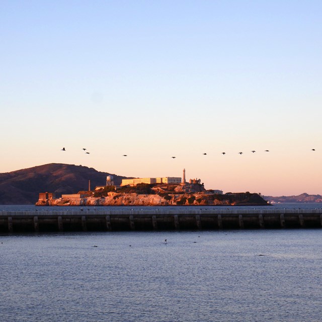 Alcatraz Island is lit with pink sunset light, viewed from Aquatic Park.