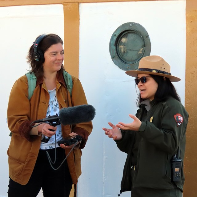 a park ranger talks to someone wearing headphones and holding a microphone.
