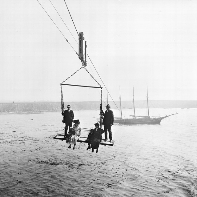 black and white photo from 1916 of two women and two men on rigging high over the water