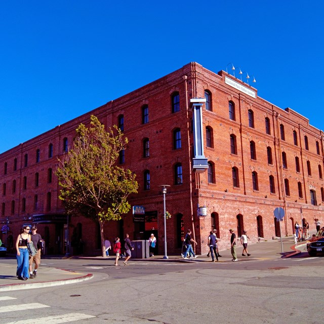 a historic brick warehouse stands on the corner of a busy street on a sunny day.