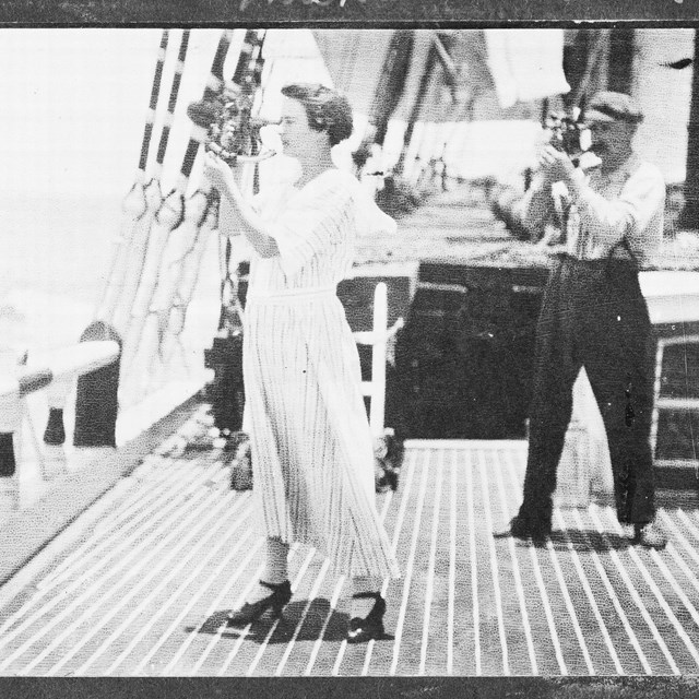 a woman in a long white dress stands on the deck of a ship holding a navigation tool up to her eye